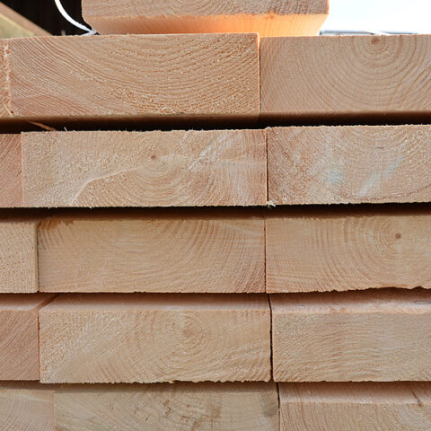 Große Stapel aus Bauholz und Holzbrettern im Außenlager Gestapelte Holzlatten und Bretter auf dem Holzlagerplatz Bauholz und Schalungsbretter ordentlich gelagert im Freien Holzbretter und Lattenpakete für den Holzbau im Lager Gelagerte Holzbretter und Bauholz vor einer Lagerhalle