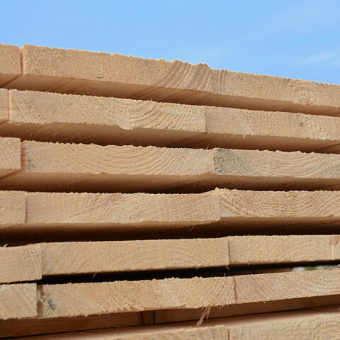 Große Stapel aus Bauholz und Holzbrettern im Außenlager Gestapelte Holzlatten und Bretter auf dem Holzlagerplatz Bauholz und Schalungsbretter ordentlich gelagert im Freien Holzbretter und Lattenpakete für den Holzbau im Lager Gelagerte Holzbretter und Bauholz vor einer Lagerhalle